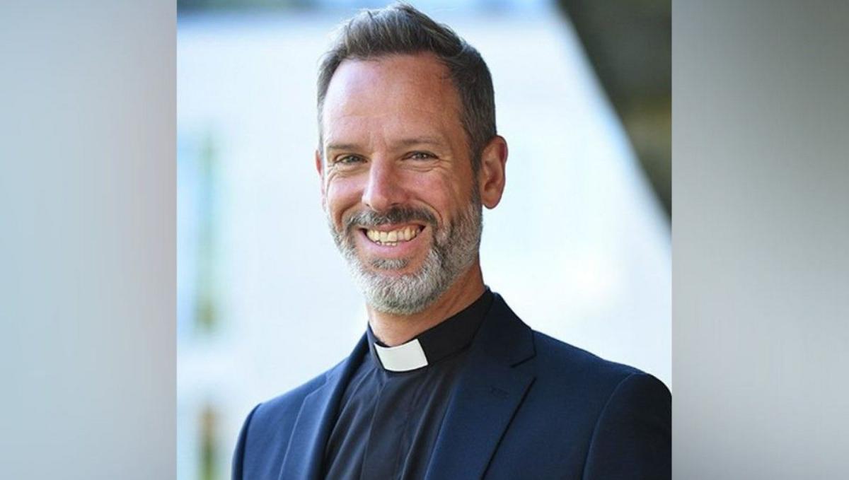 Rt Revd Dr Michael Volland is facing the camera and smiling. He has a grey beard and dark hair and is wearing a dog collar and blue jacket.