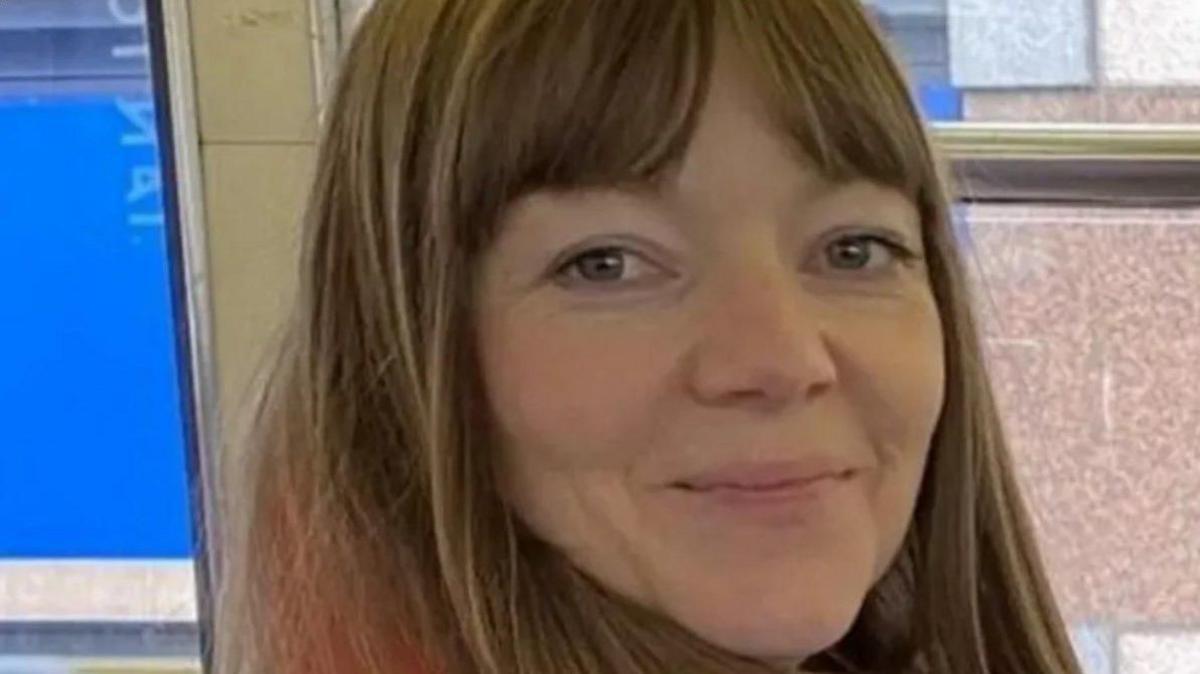 Joanne Samak, a woman with long light brown hair, smiles at the camera.