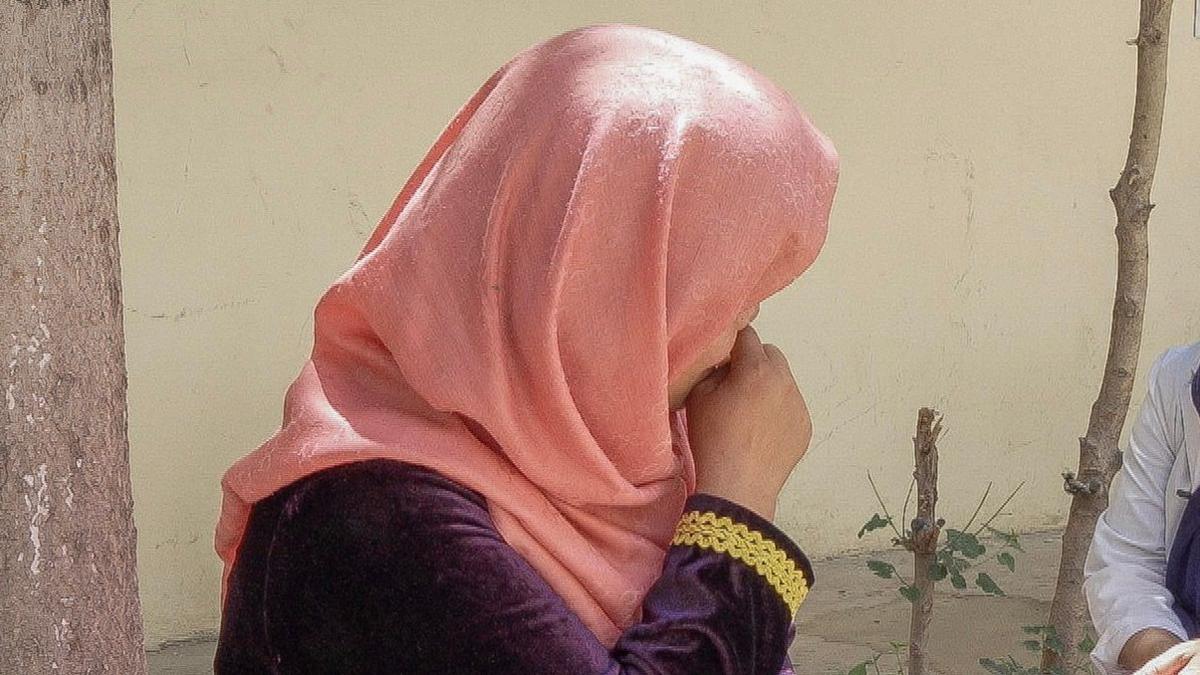 Closeup of profile of the face of a woman wearing a pink headscarf, her hand covering her mouth.