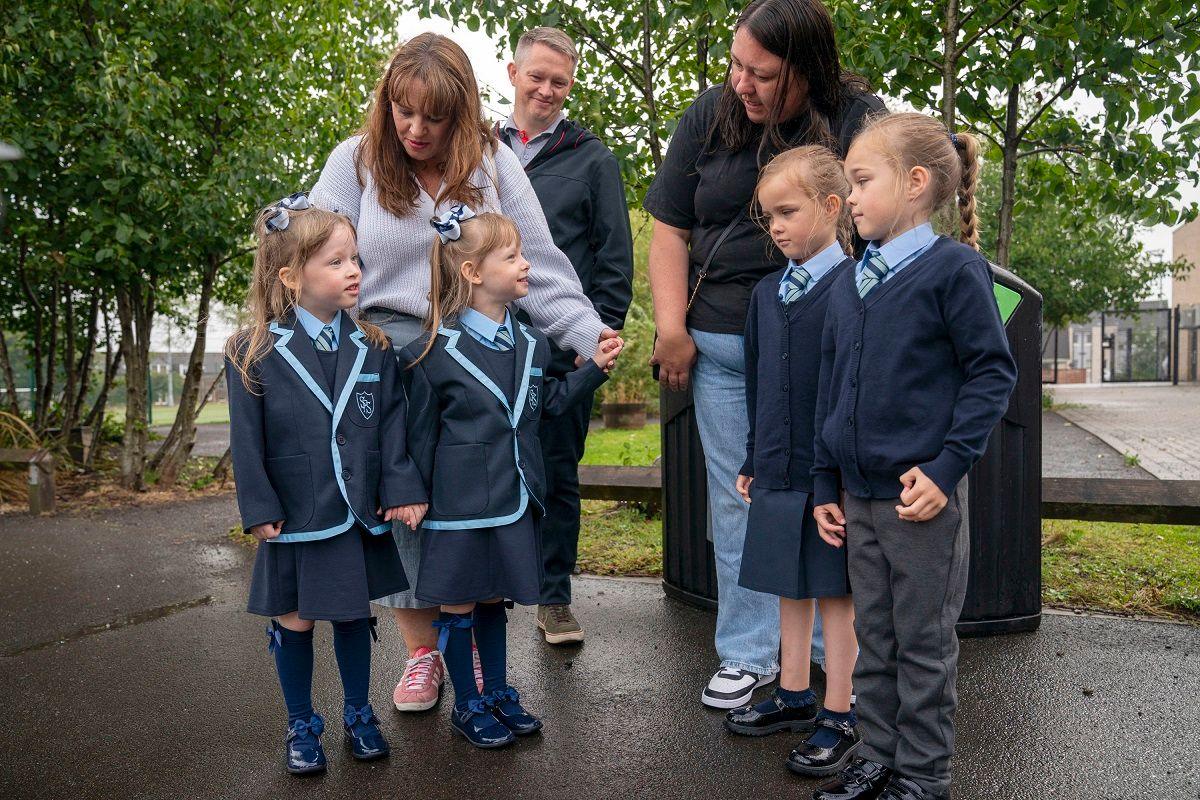 two sets of twin sisters meeting one another outside school with their parents