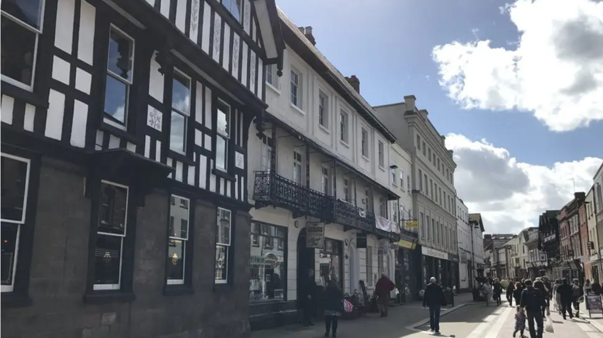 A row of shops of varying ages with customers outside 