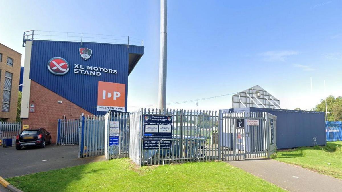 Outside view of the blue Coventry Rugby Club stand showing the signage 'XL Motors Stand' and the crest of the club.