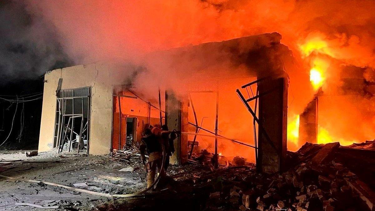 A fire service person uses a fire hose to douse the flames on a burning building