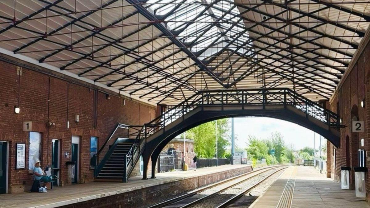 The interior of Filey railway station - a red brick building with two railway tracks running through, and a platform either side. An iron bridge spans the two platforms.