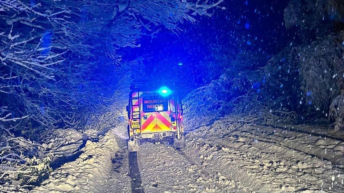 A mountain rescue vehicle pictured from behind while going up a very snowy track at night