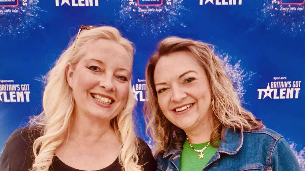 Two women, including Lisa Skinner on the left, standing in front of a blue backdrop with the Britain's Got Talent logo on it. They are both smiling into the camera.