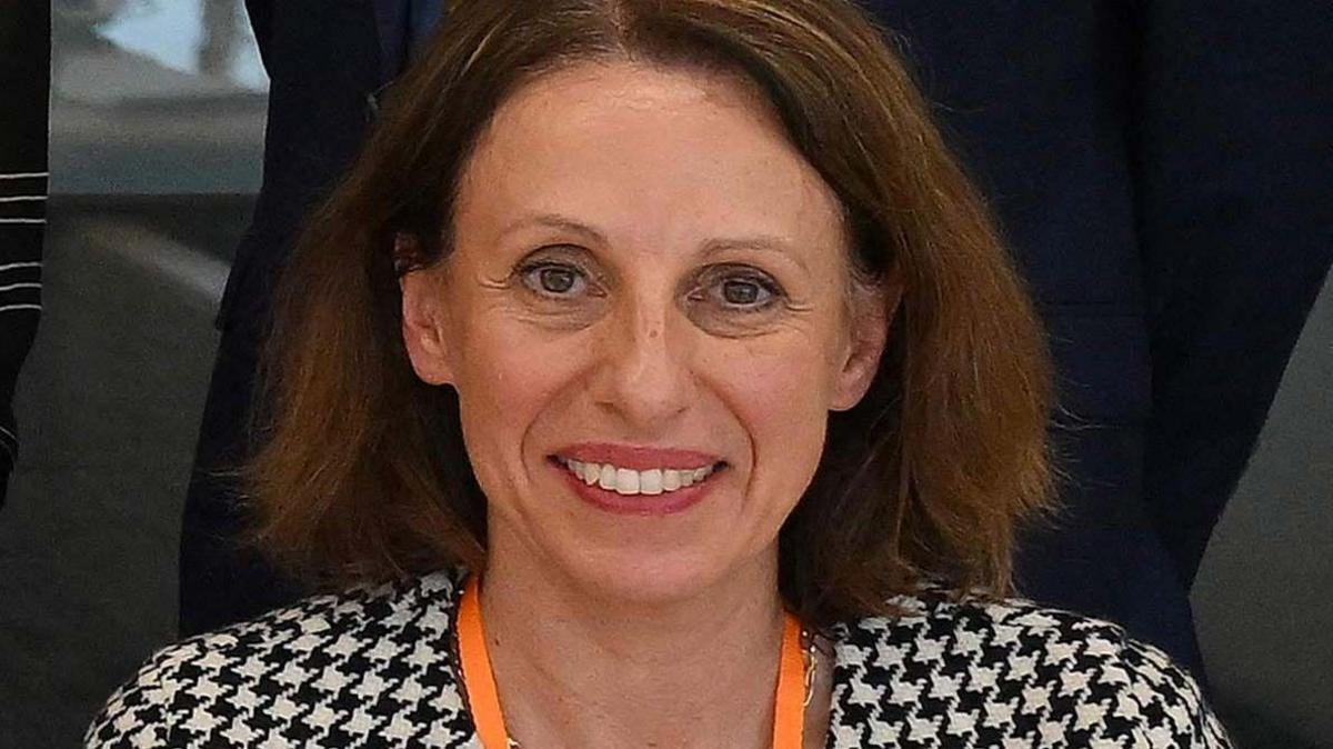 Shirine buzëqesh ndërsa mban veshur një xhaketë të zezë dhe të bardhë si gjuetar dhe një litar portokalli.