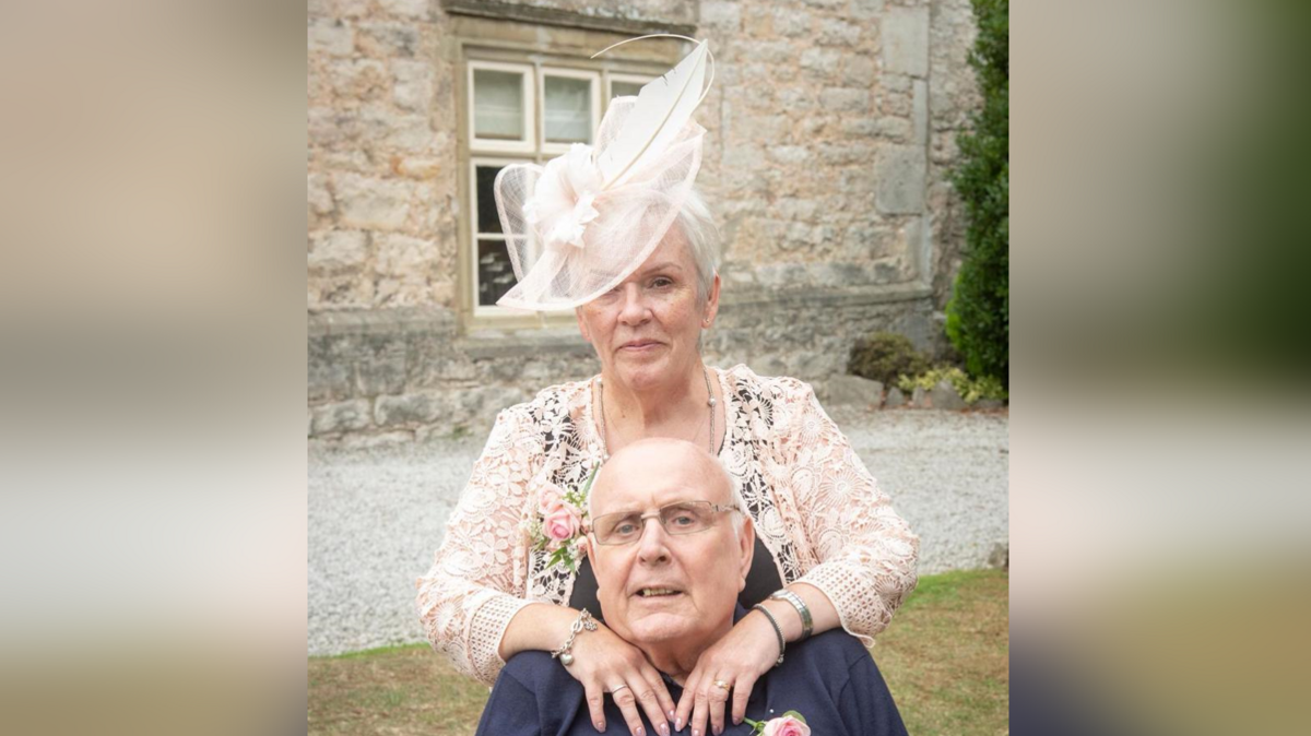 A woman stands outside with her arms on a man's shoulders. They are both dressed in formal wedding attire