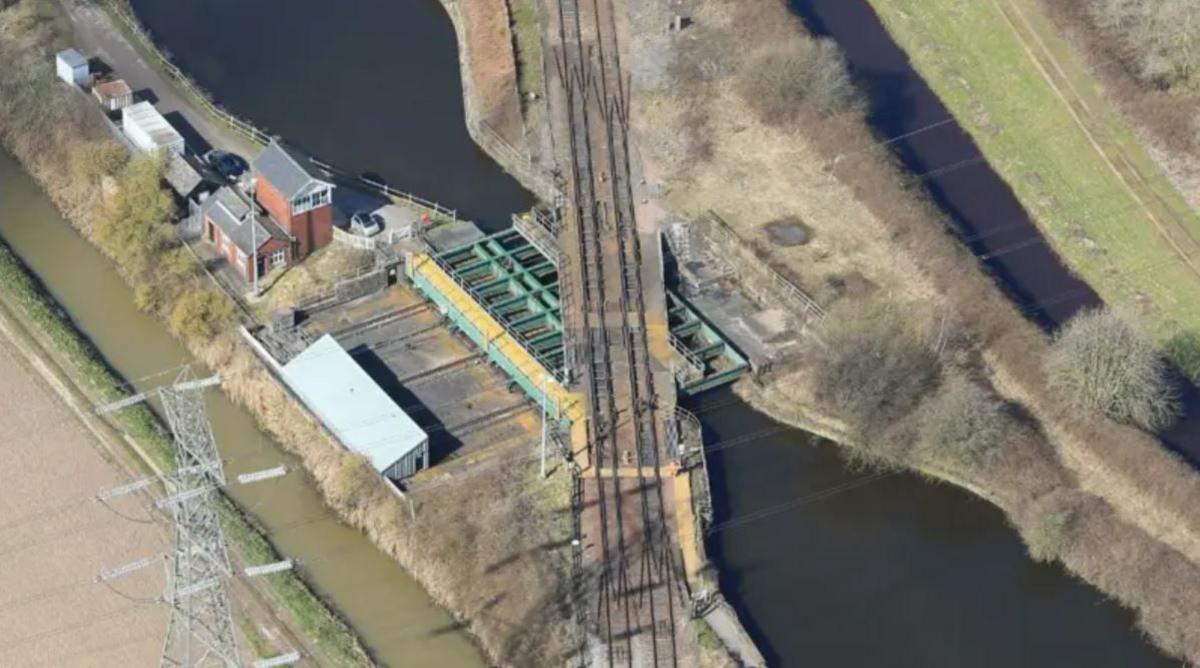 An aerial view of train tracks going across a bridge, which sits above a waterway.
