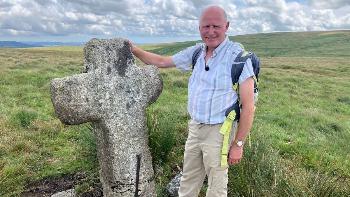 Author Nick Pannell standing on Dartmoor with his hand on a medieval cross