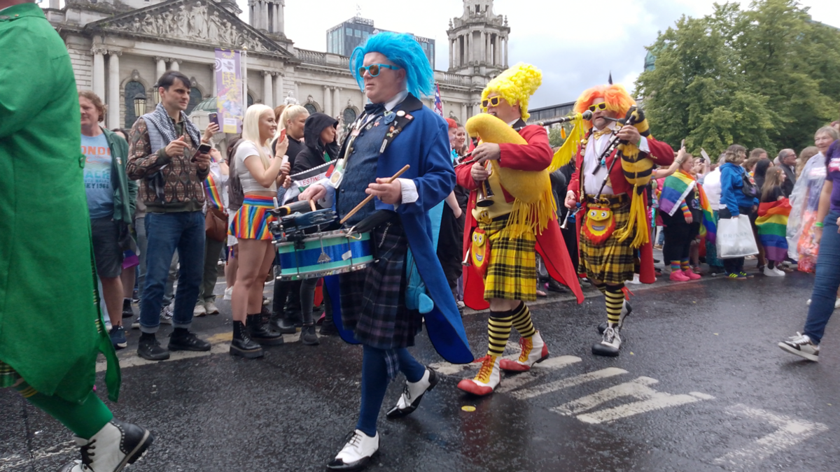 People wearing colourful wigs and kilts walk in the parade playing drums and bagpipes