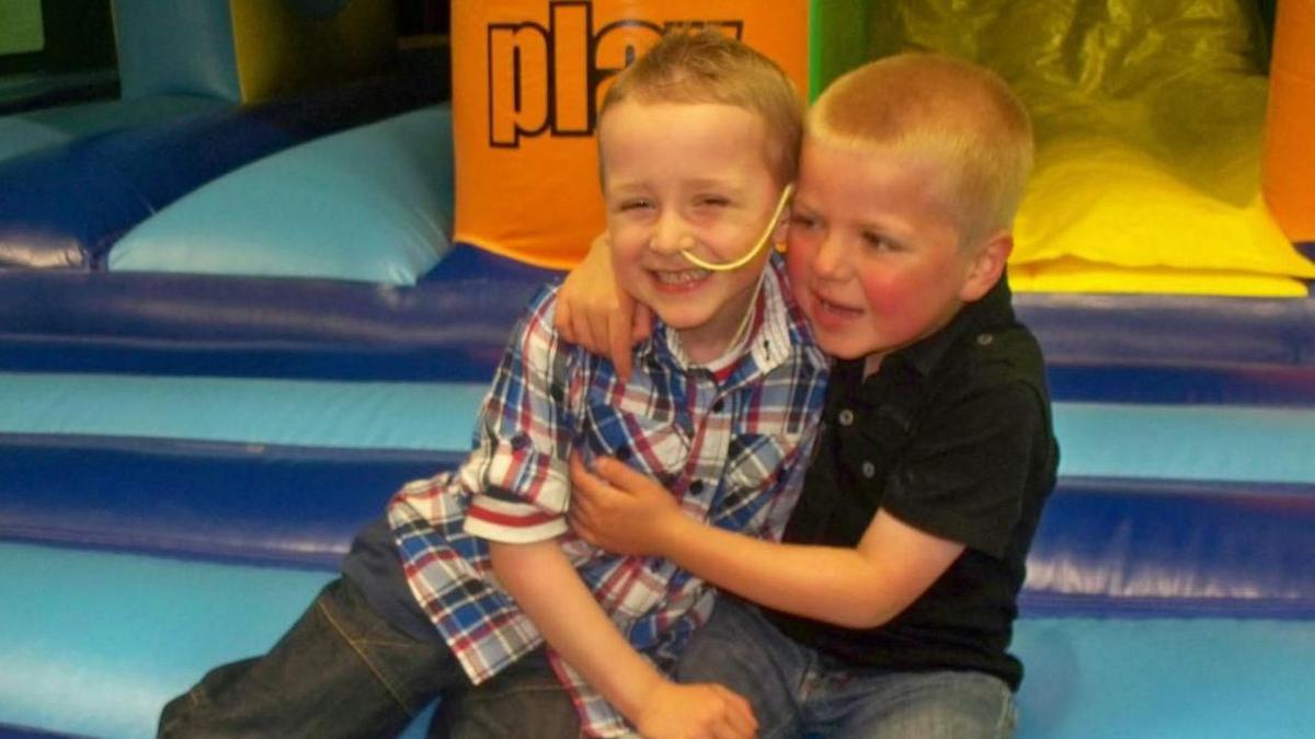 two small blond-haired boys hug in a soft play area