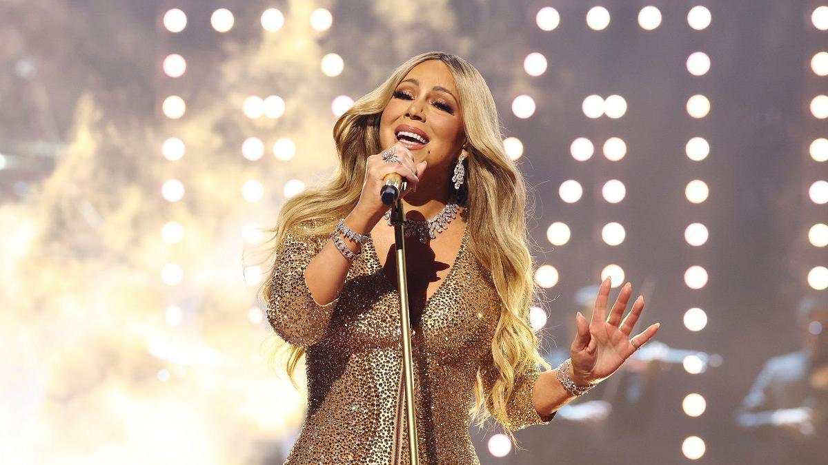 Mariah Carey performing wearing a gold sparkly dress