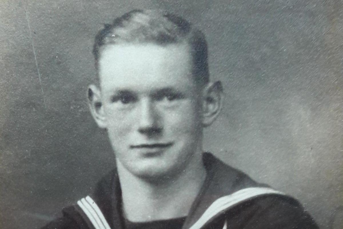 Bill Redston in a black and white image dressed in a Royal Navy uniform. He has short, dark hair with a side parting and is clean shaven.