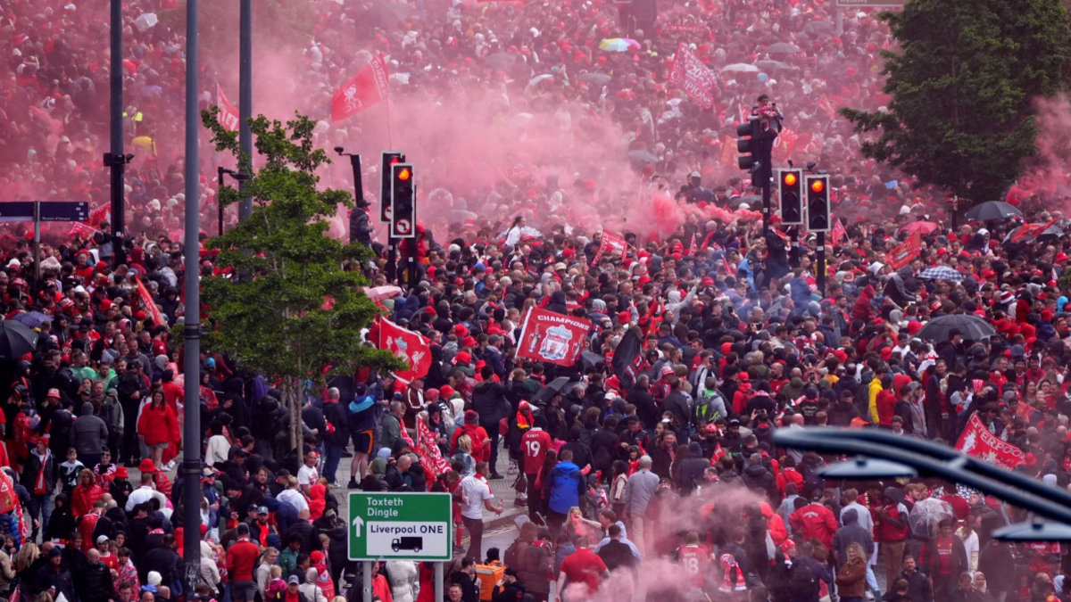 Hundreds and thousands of Liverpool fans, mainly in red t-shirts on the streets of Liverpool. There are red flares of smoke seen.