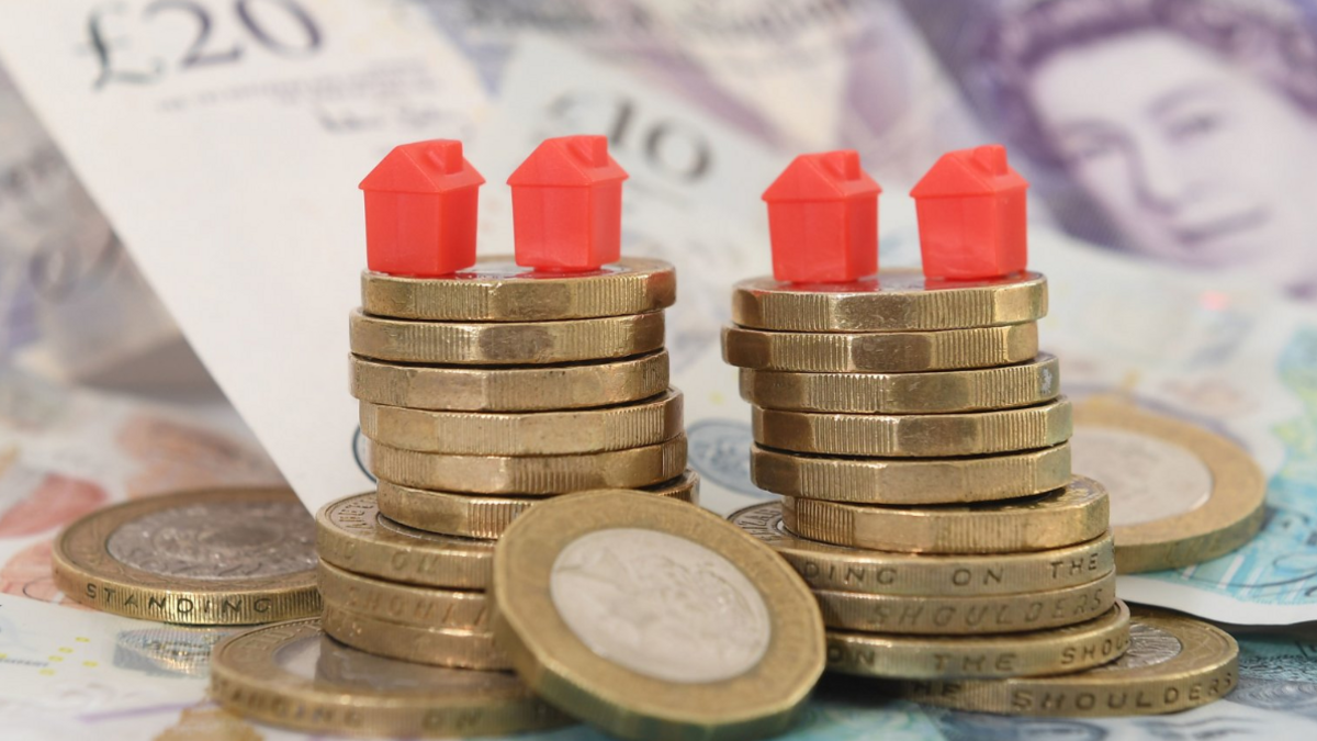 Piles of pound coins on top of bank notes, topped with four red Monopoly houses