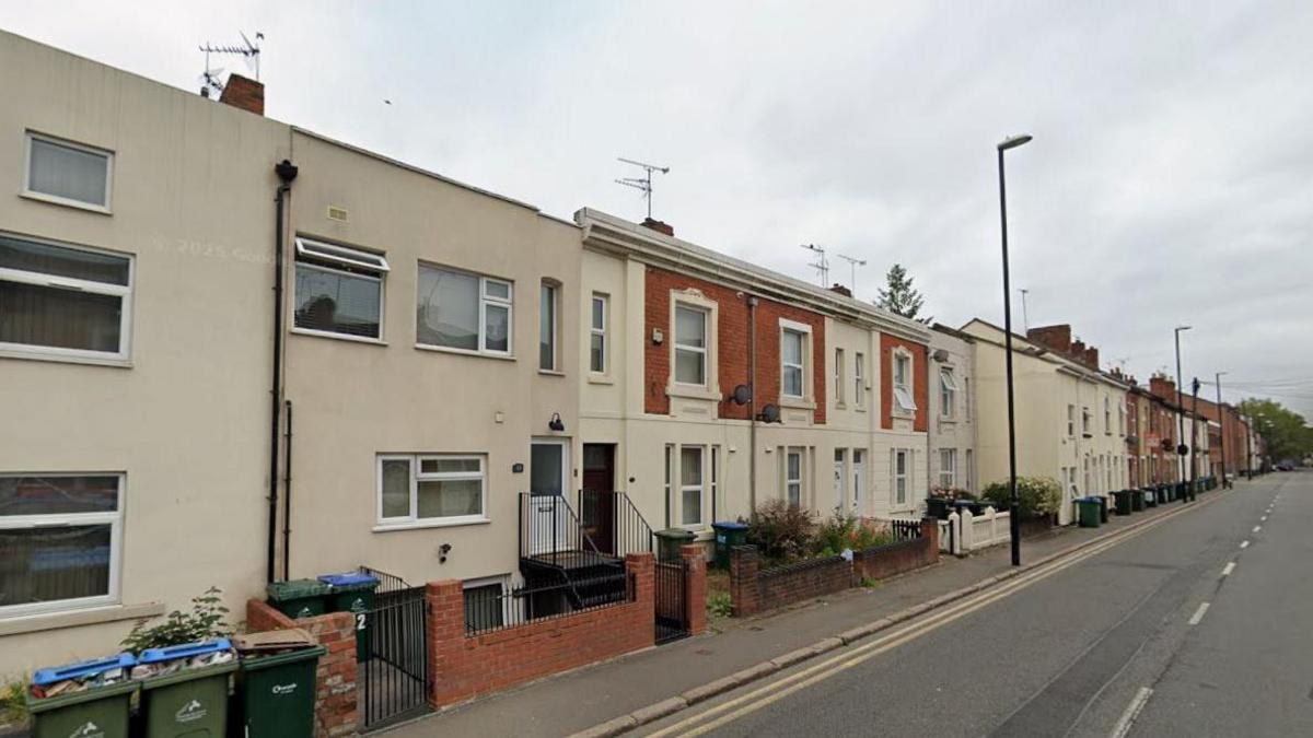 A Google image of Lower Ford Street in Coventry. The road has terraced houses on both sides in cream and red brick. There are steps leading up to some properties and many of the houses have bins in front of them.