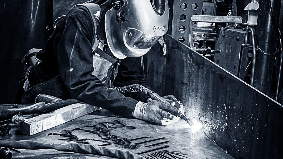 A man wearing protective gear who is using a welding electrode to create a sculpture out of steel.
