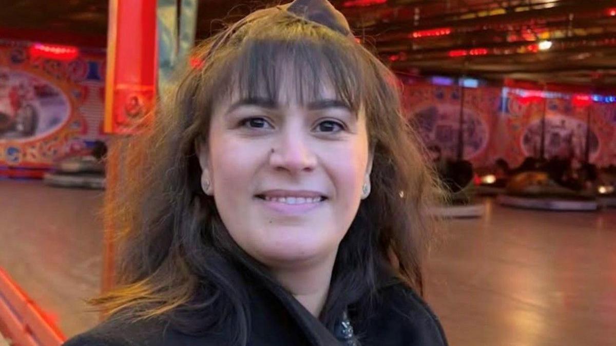 Nihal with dark hair and a fringe, smiling at the camera, standing in front of bumper cars at a fairground