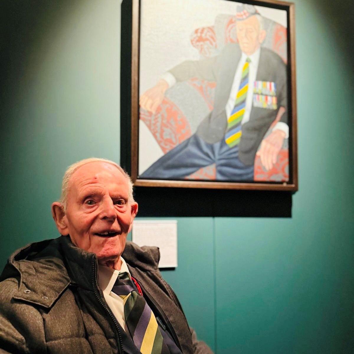 Jim Glennie, 99-year-old man wearing a striped tie and a jacket, in front of a portrait of himself.