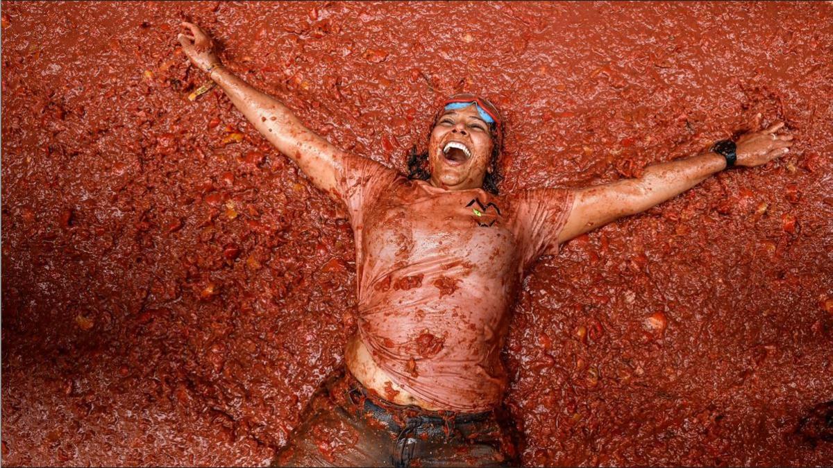 A woman lying back in a pool of tomatoes with a smile on her face 