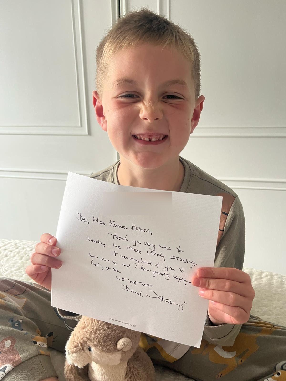 Max, who has short blond hair, holding up a letter with handwriting on it.