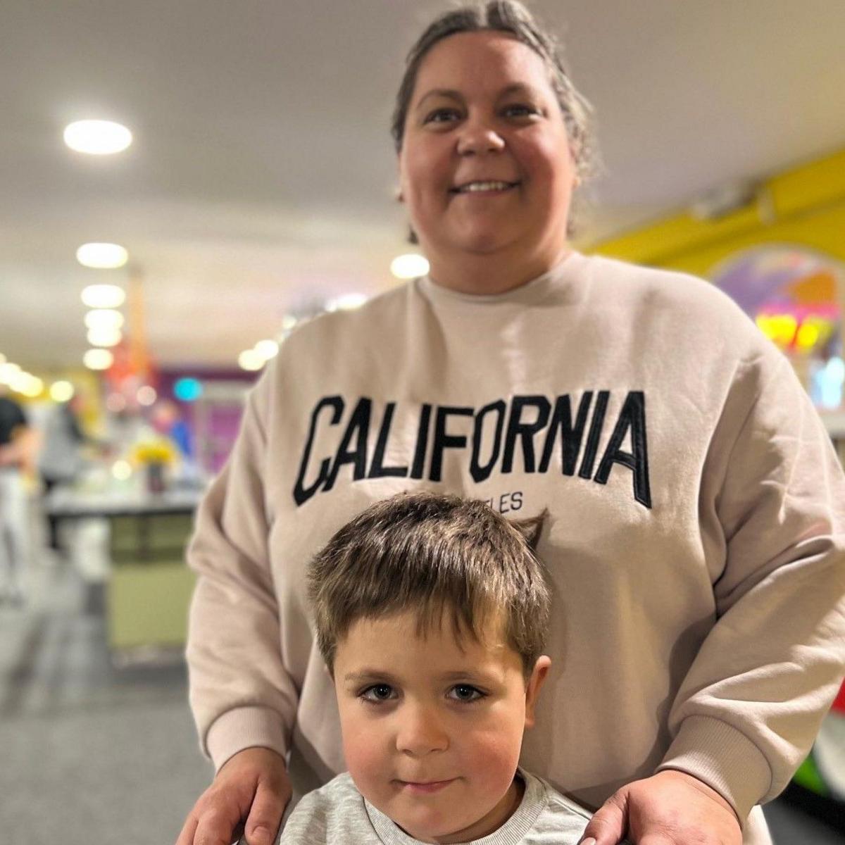 Kristina Fletcher, wearing a baggy sweatshirt with her fair hair tied back, standing in a soft play centre with her hands on the shoulders of her four-year-old son Magnus