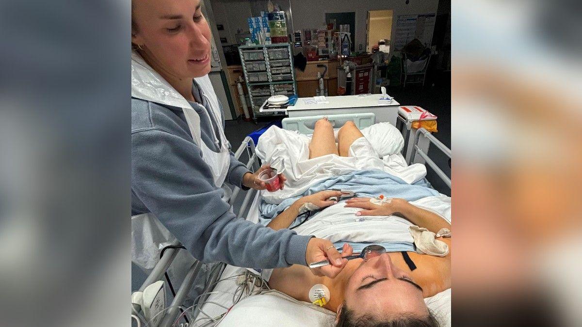 Emma lying on her hospital bed with medication and drips attached to her, while a friend spoon-feeds her.