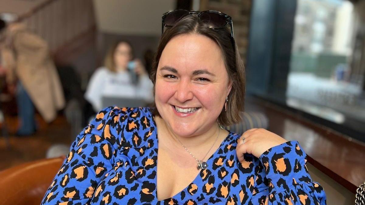 A woman is pictured in a blue leopard print top while smiling in a coffee shop