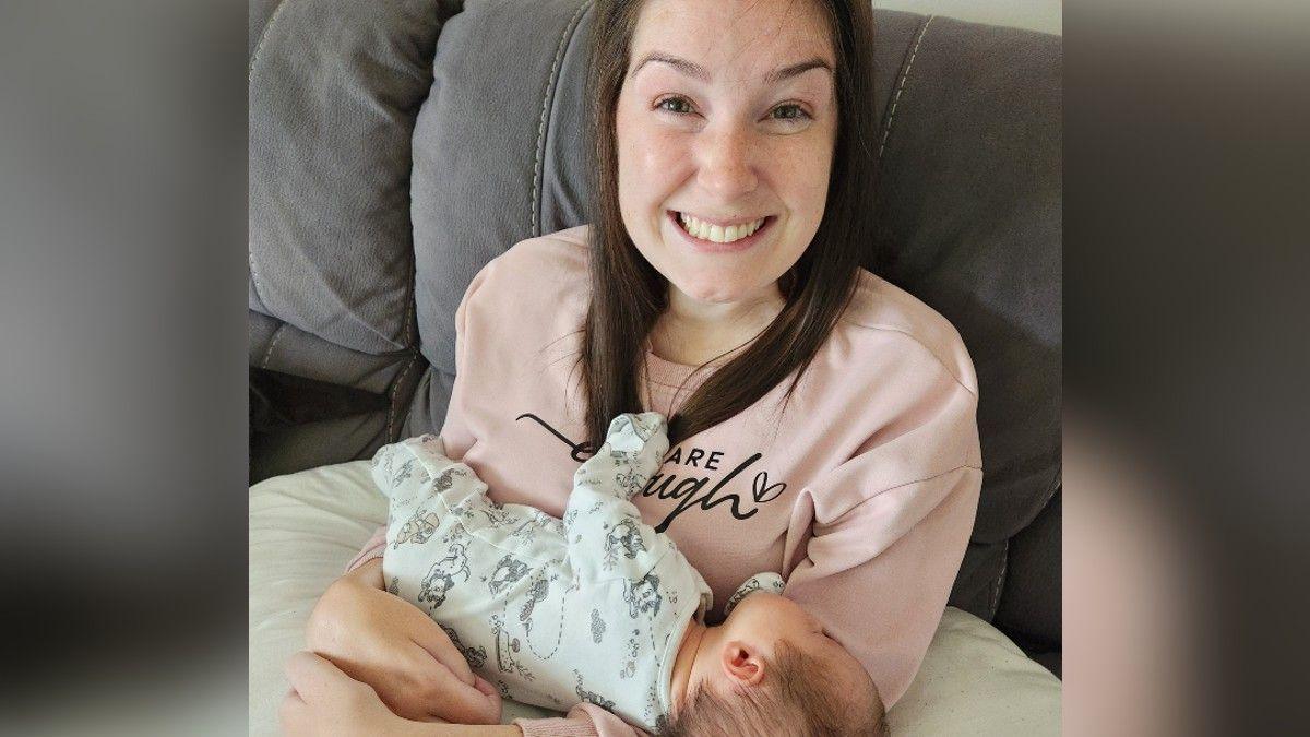 Lucy Lintott Smith holds her sleeping baby who is supported on a pillow