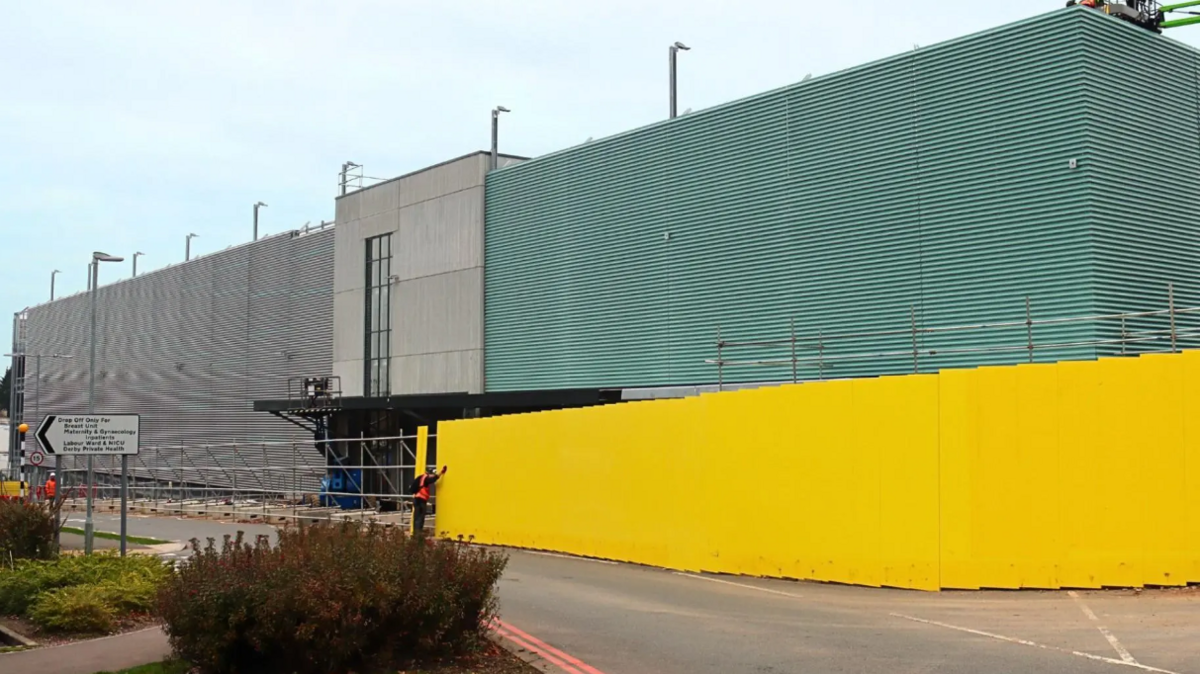 A silver and green clad multi-storey car park, with yellow fencing outside the front