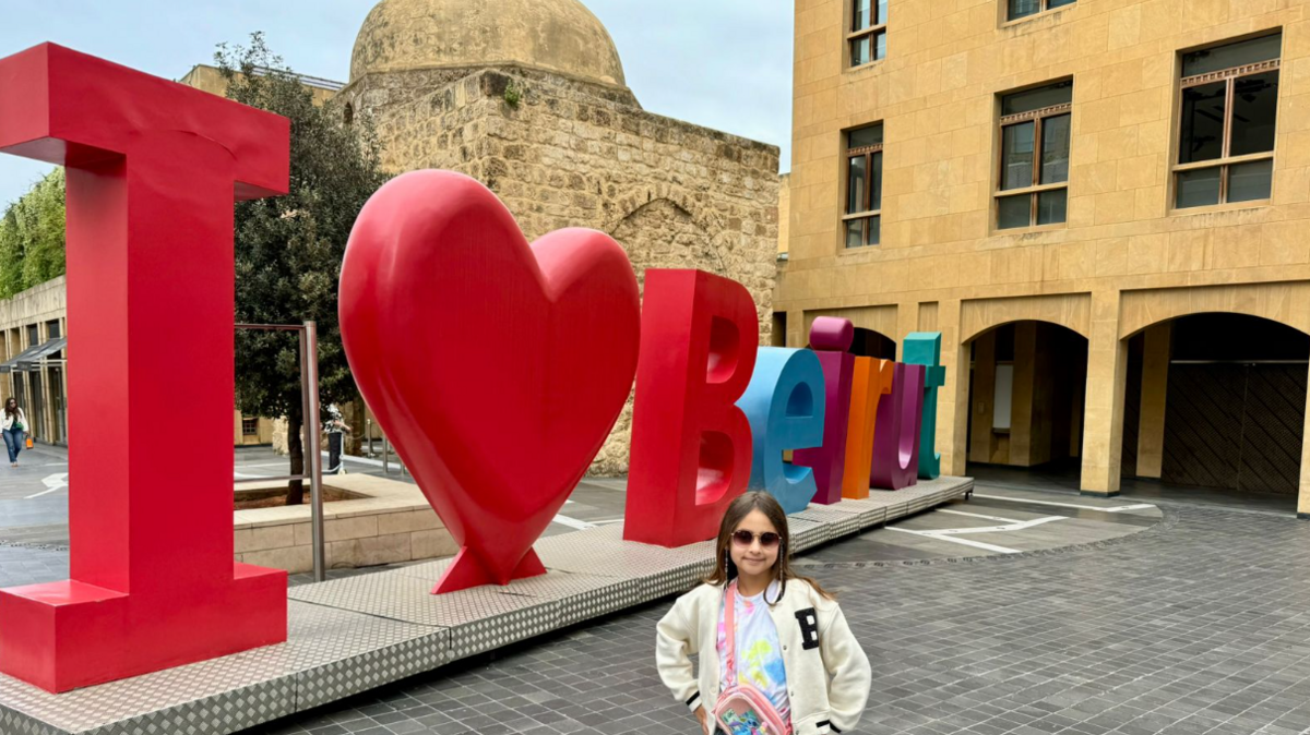 Dan Harper's daughter standing next to a Beirut city landmark that reads I love Beirut