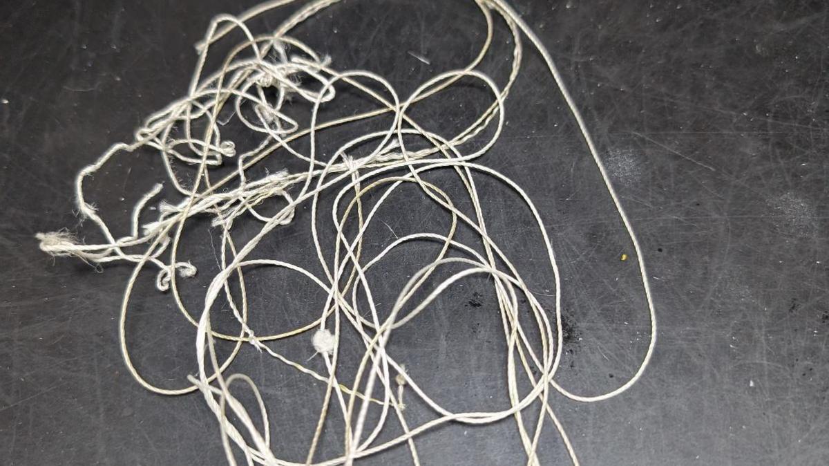 A white length of string tangled up on a table with a black surface.