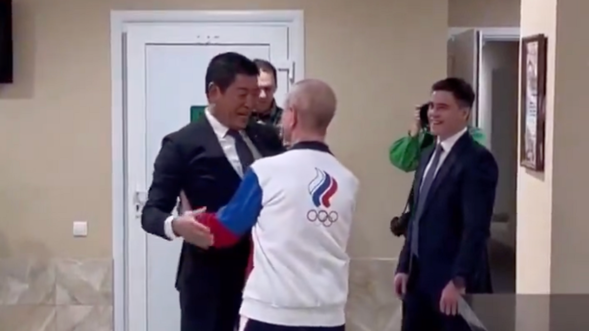 Morinari Watanabe is being greeted by someone in Russian sports kit while Nikita Nagorny waits to meet him