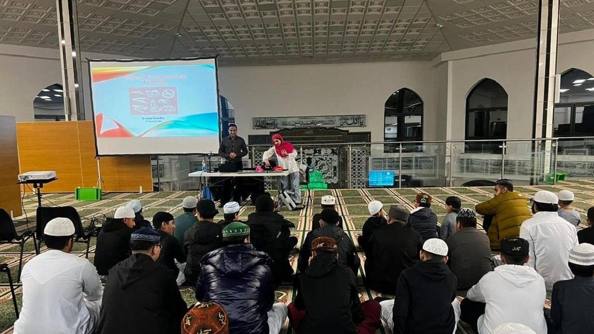 Chidlren wearing white skull caps sitting on the floor in fornt a projector inside a mosque