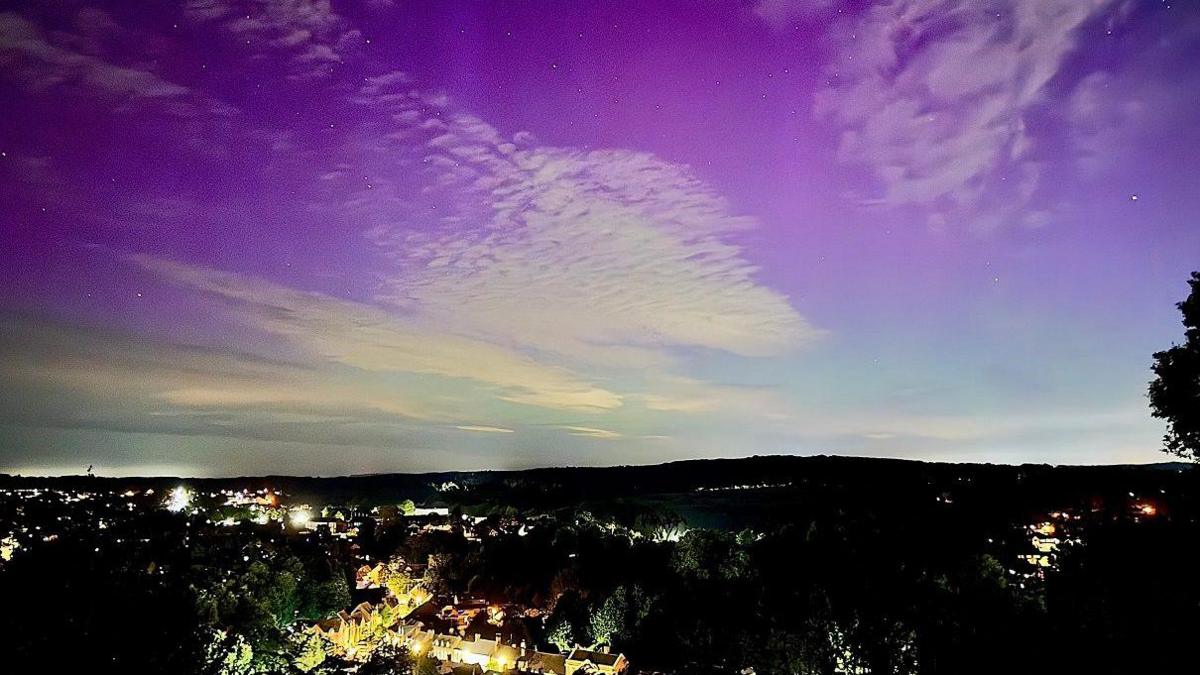 Purple lights above a town in the night sky with clouds visible