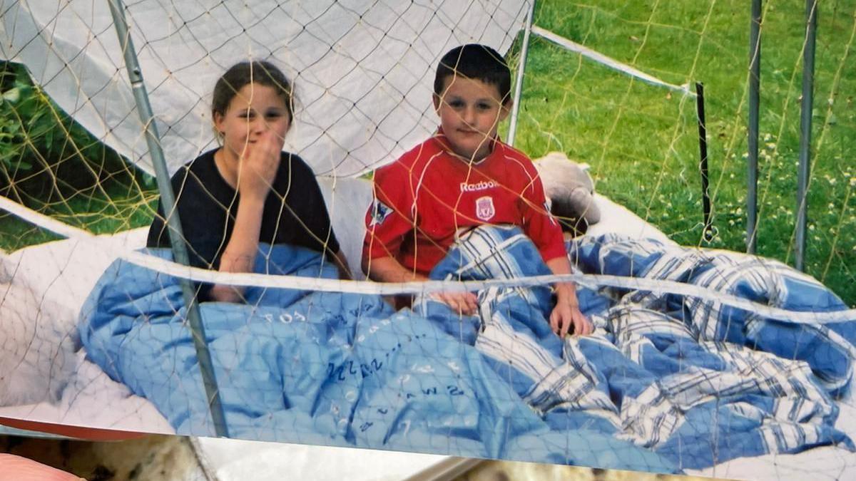 An old image of Tom and his sister as children sitting in a garden under a duvet in a sort of fort smiling and looking at the camera