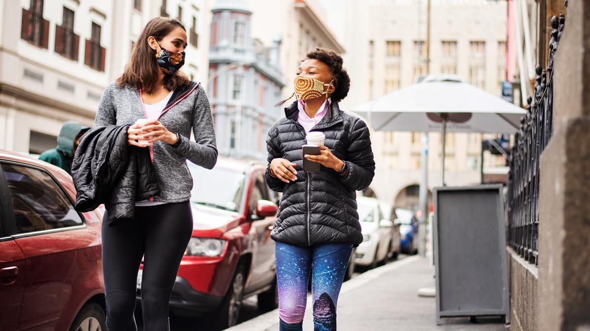 Two women in a street wearing masks and carrying coffee cups