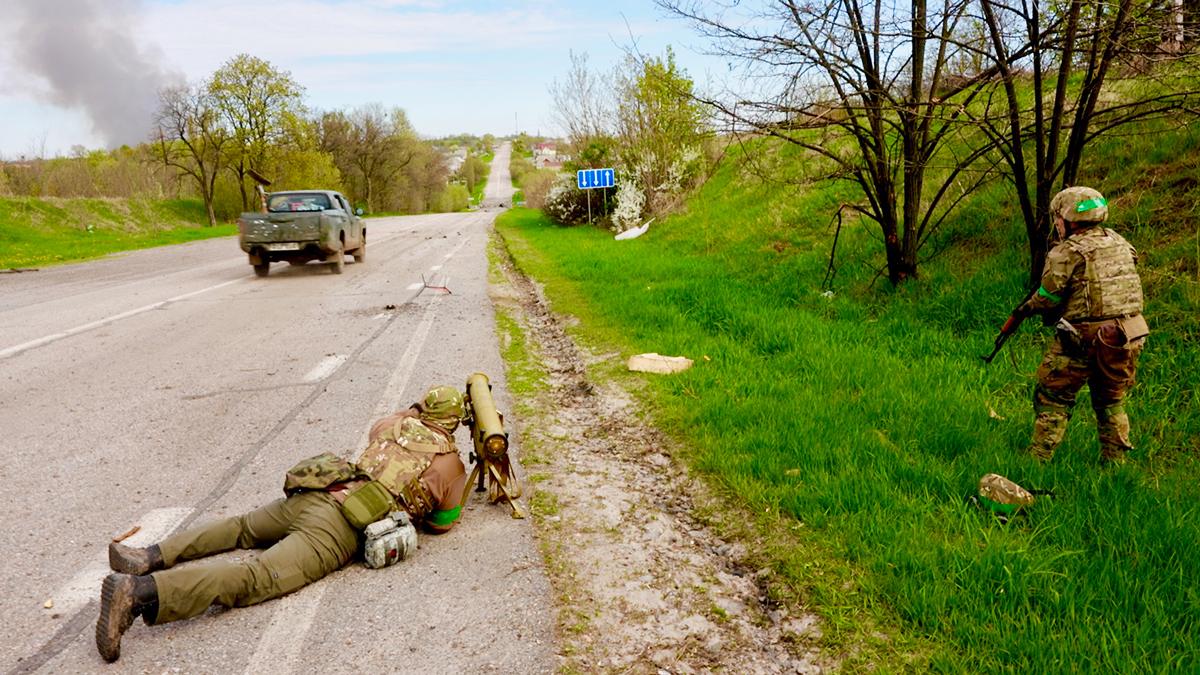 With Ukrainian troops by a roadside to the north of Kharkiv, smoke visible in the distance