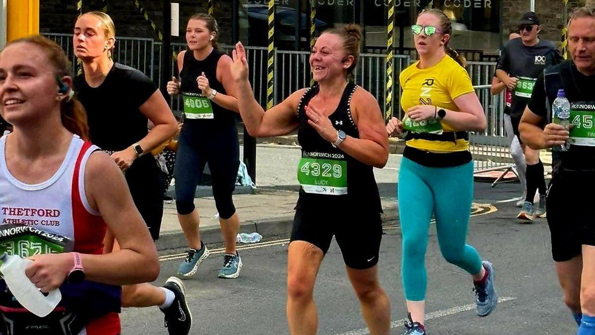 Lucy taking part in Run Norwich surrounded by other runners and waving 