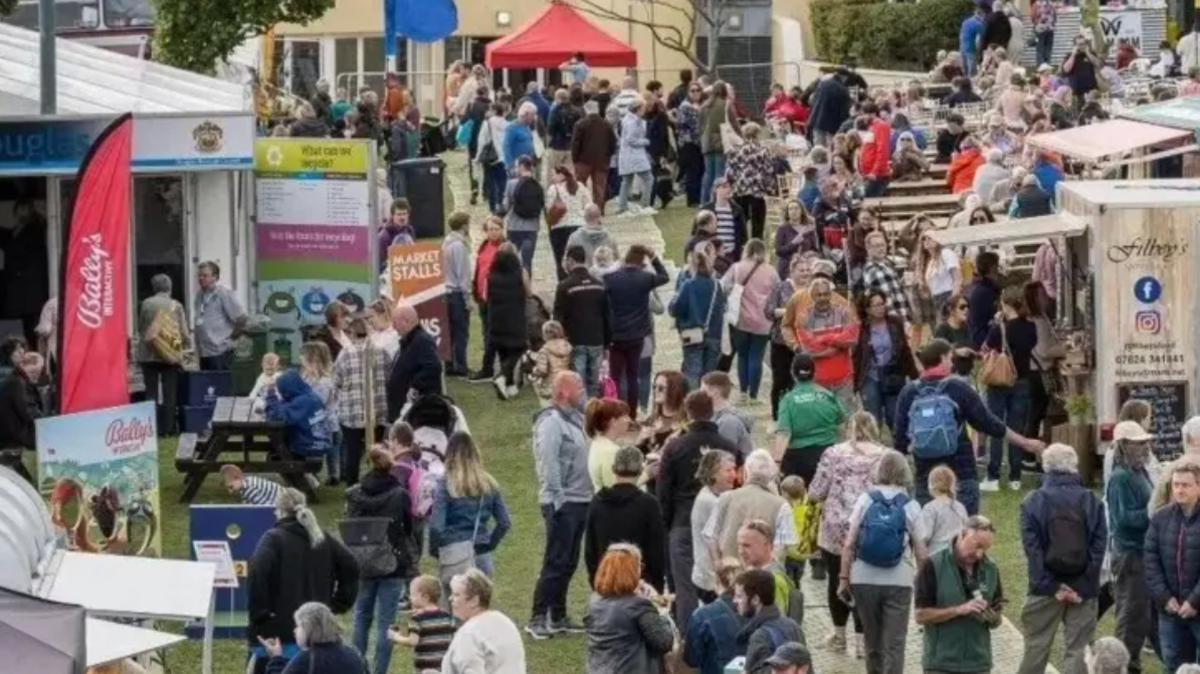 Wide shot of the Isle of Man Food and Drink Festival. People are milling around in between food and drink stalls outside.