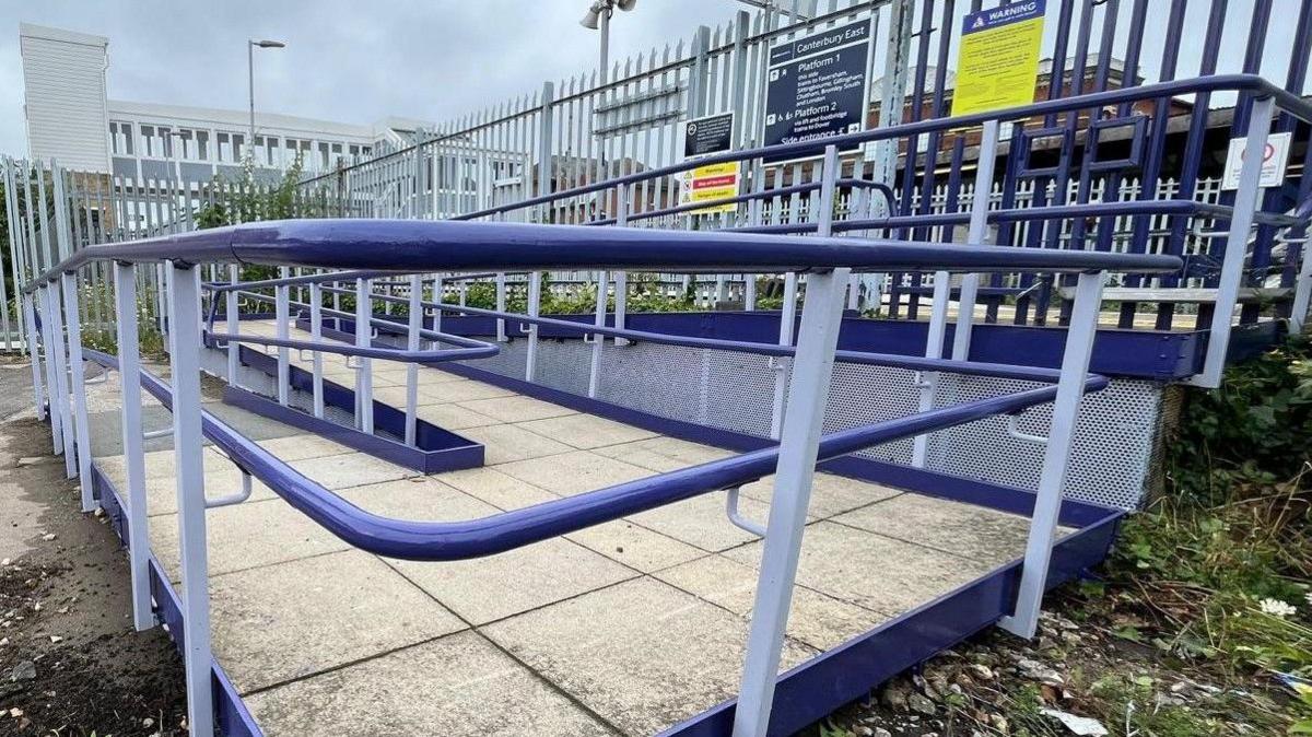 A ramp with blue hand rails leading up to platform one at Canterbury East station