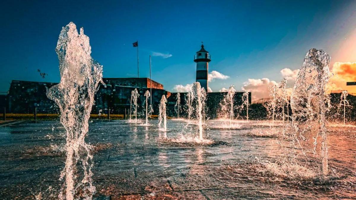 Water fountains spring up from the ground beneath Southsea's skyline, which contains its lighthouse and a silhouetted flag