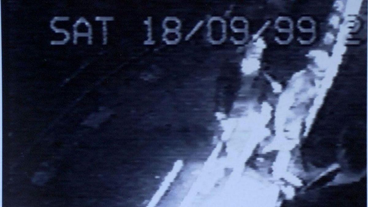 Grainy black-and-white CCTV image shows two young women walking from the road into a nightclub. A doorman, dressed in suit and tie, looks at them as they enter. A digital caption across the top of the image reads: "SAT 18/09/99".