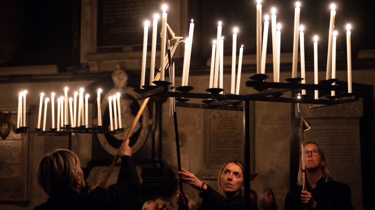 A close up of three people lighting dozens of candles in darkness in Salisbury Cathedral