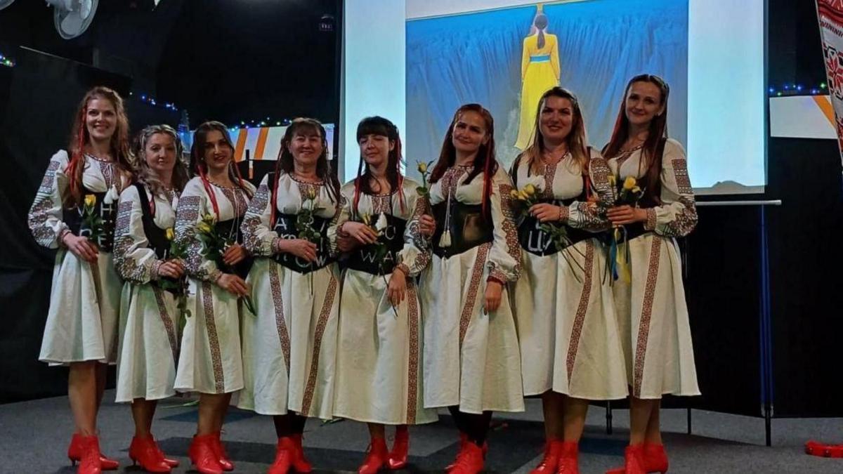 The Dorset Ukrainian women from the community group are dressed in white, black and red dress (traditional Ukrainian dress) with red shoes. They are all holding yellow tulips.