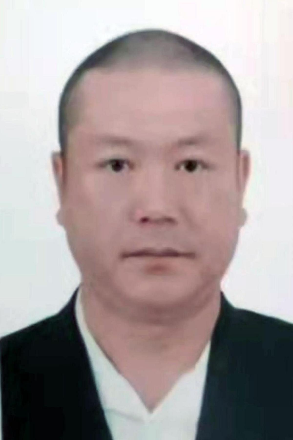 A headshot of the victim, Chinese national, Jinming Zhang. The image is a passport photo. He is staring seriously at the camera and is wearing a white top and black jacket over the top. He has short black hair.