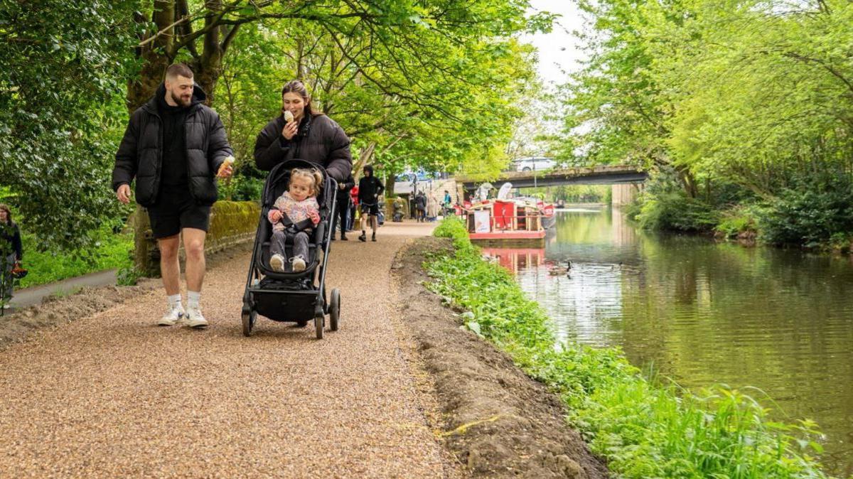 A couple pushing a pram along a section of the towpath near Saltaire that has already been upgraded by Sustrans