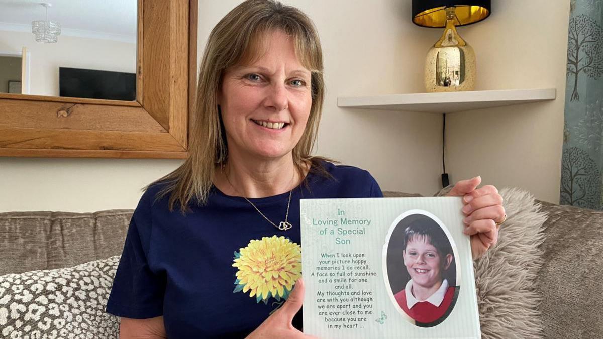 A woman holding of a card with a photo of a young boy in school uniform printed on it