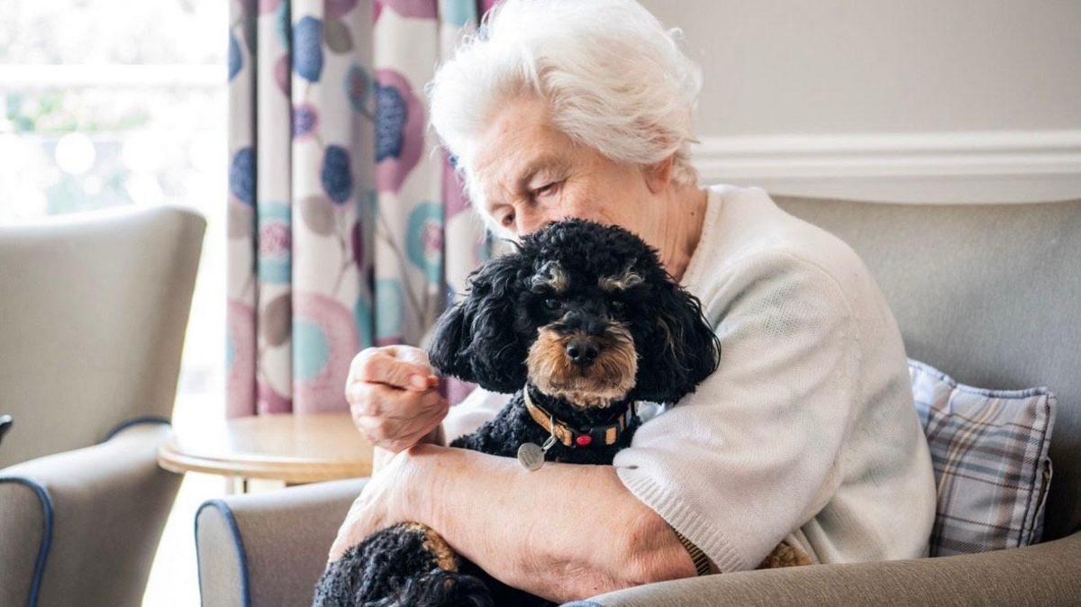 A resident cuddles a dog on the sofa.